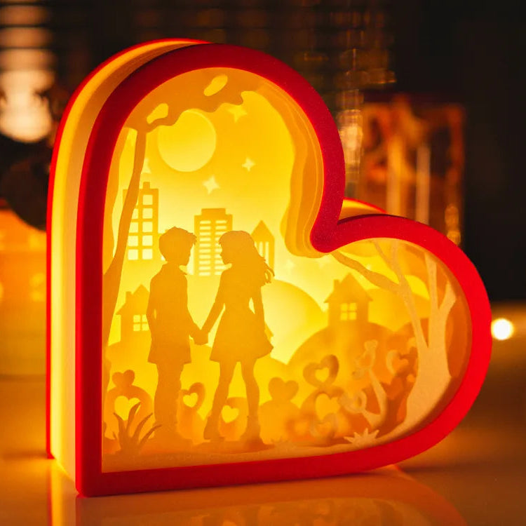 Heart-shaped LED lamp with a silhouette of a couple and teddy bear inside, glowing warmly.