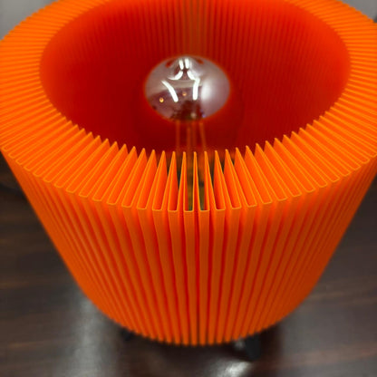 Close-up of an orange pleated lampshade with a visible light bulb inside.