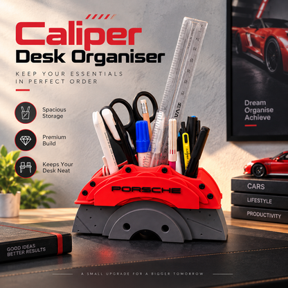 A red and gray Porsche-branded desk organizer shaped like a brake caliper, holding pens, a ruler, and scissors on a desk. The scene includes promotional text reading 'Caliper Desk Organiser' and a framed sports poster in the background.