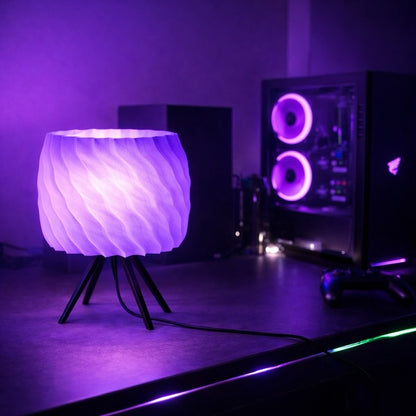 Lamp with wavy design on a stand in a room with computer equipment and purple lighting.
