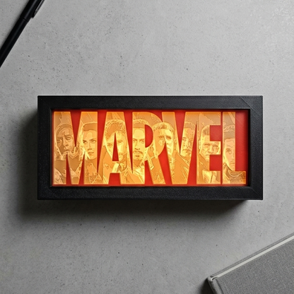 Framed Marvel logo with a pen and notebook on a gray surface