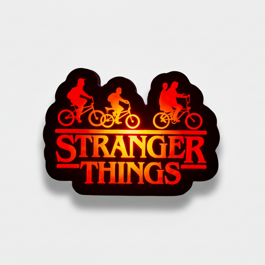 Decorative sign with 'Stranger Things' theme featuring silhouettes of characters on bikes against a dark background.